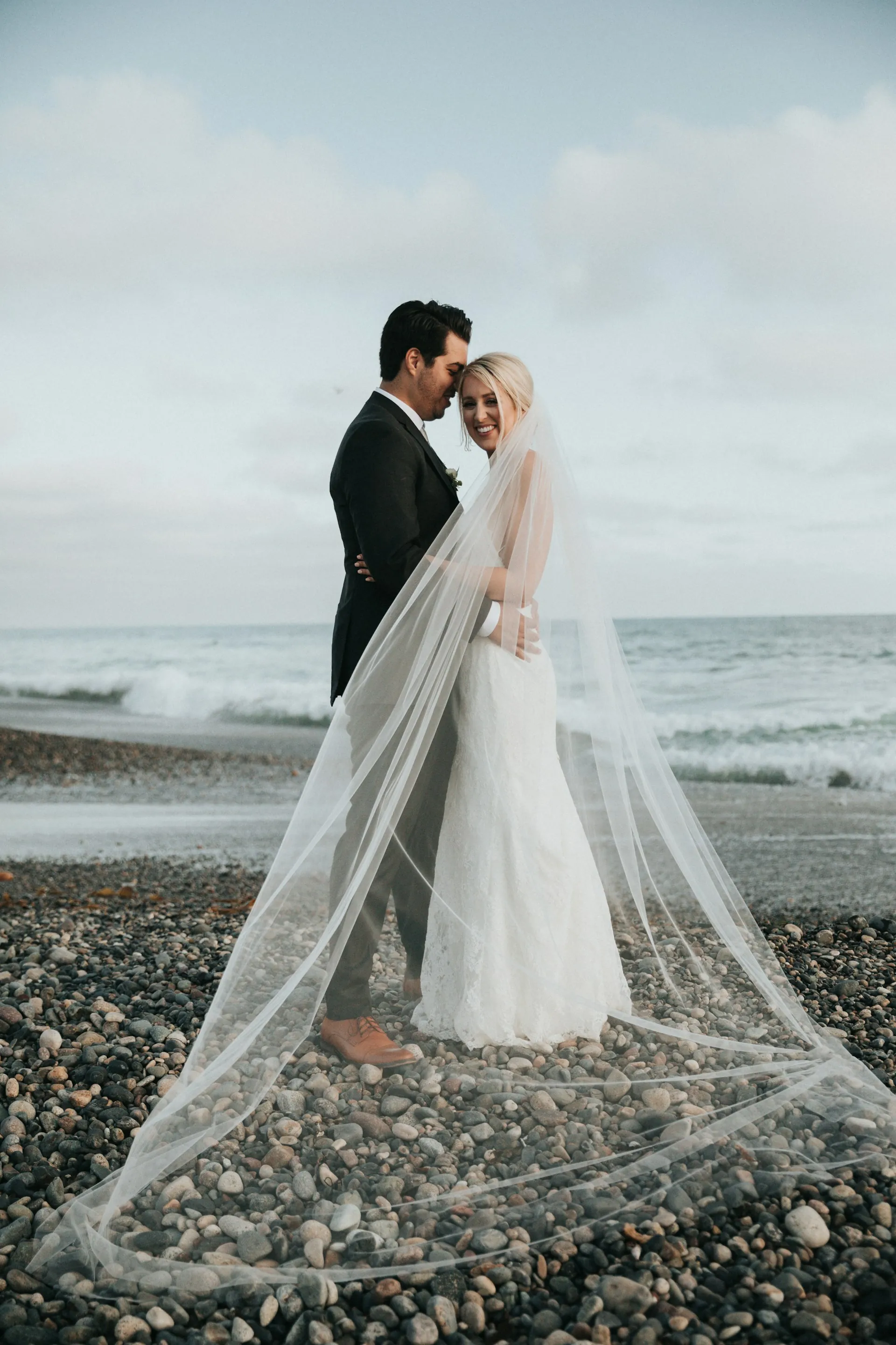 A couple on a pebble beach, her veil caught in the wind