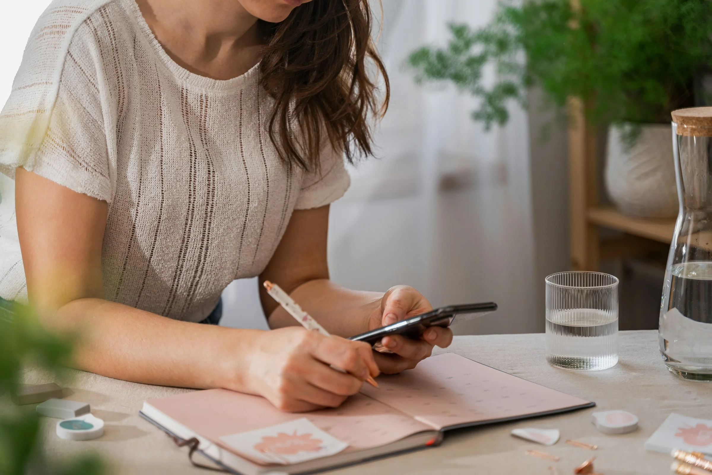 A planner writing in a paper planner, phone in hand
