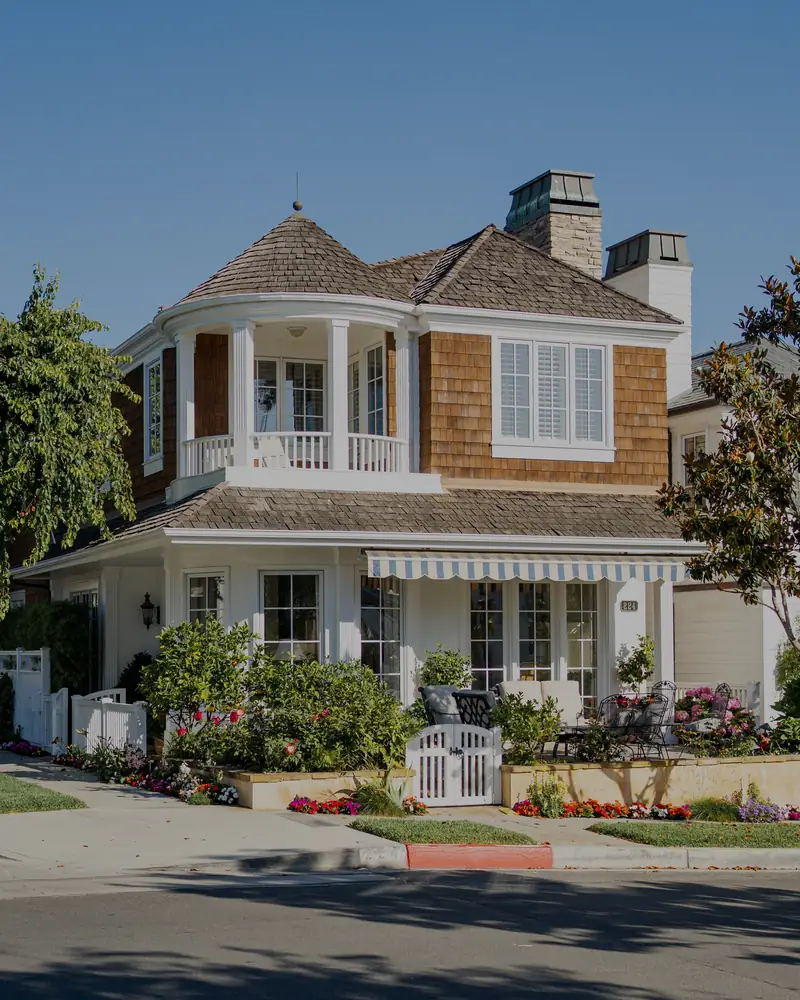 A shingled beach cottage with a white porch, on a sunny street